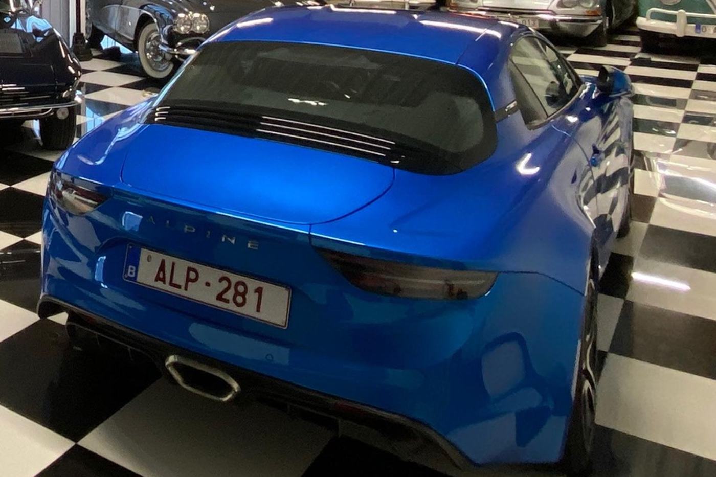 Alpine A110 bleue de 2018 vue de trois quarts arrière dans le garage DeVinCi au sol en damier
