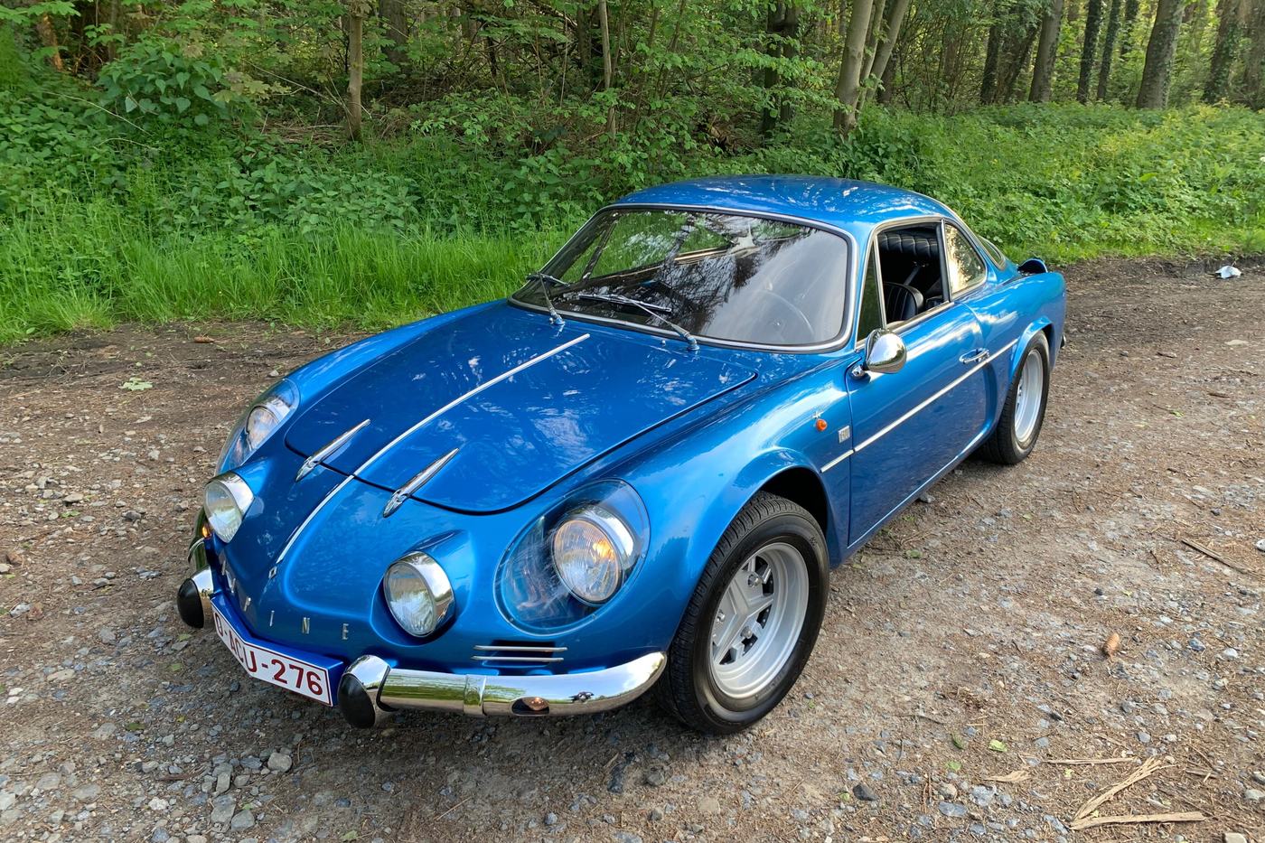 Alpine A110 1300 berlinette bleue vue de trois quarts avant sur un chemin en forêt