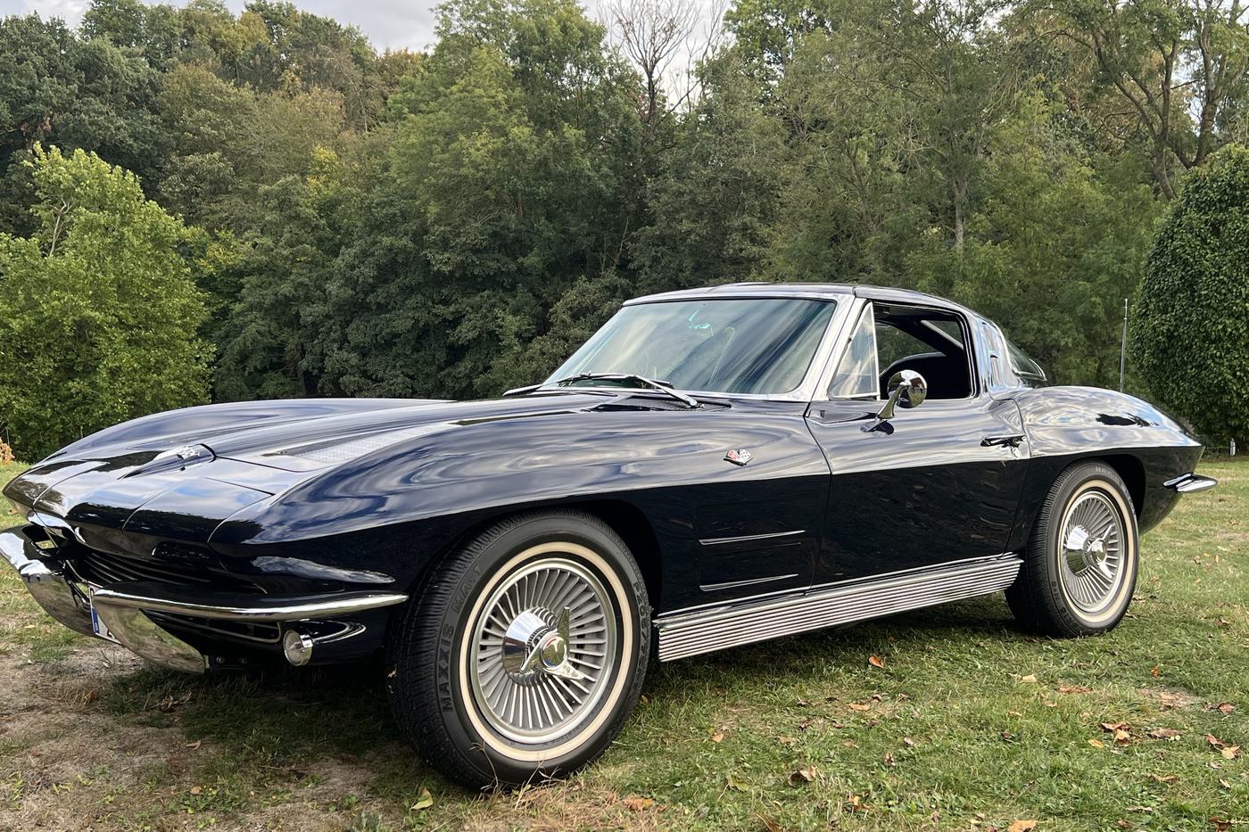 Corvette C2 Sting Ray bleu foncé de 1963 vue de profil sur une pelouse bordée d’arbres