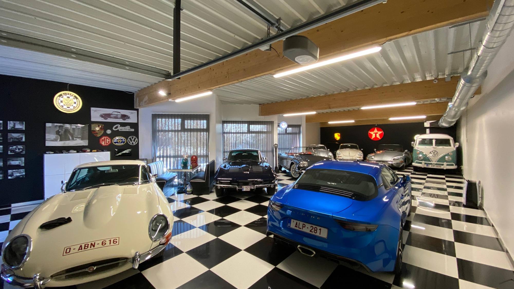 Le garage DeVinCi : une Jaguar Type E blanc cassé et une Alpine A110 bleue sur un sol en damier noir et blanc