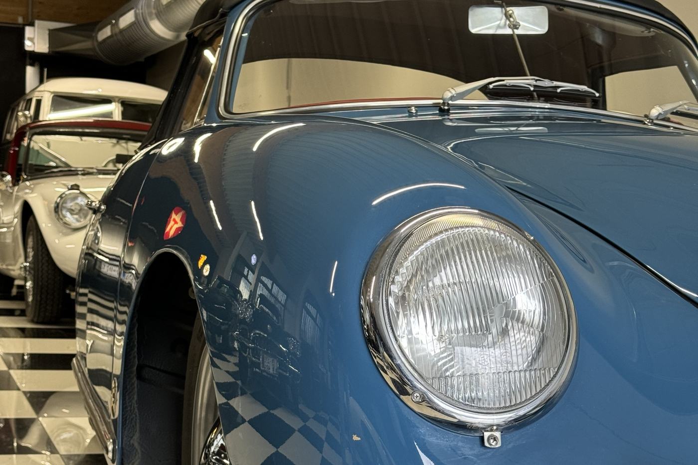 Aile avant et phare rond d’une Porsche 356 A 1600 Super bleue, en gros plan dans le garage DeVinCi