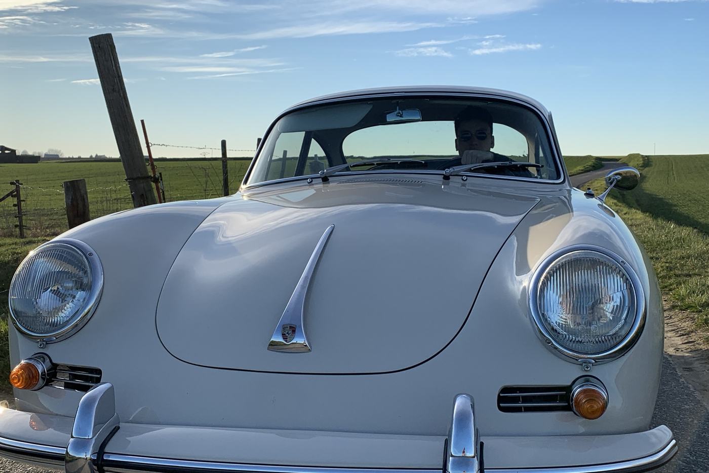 Face avant d’une Porsche 356 B blanc cassé de 1962, phares ronds et capot plongeant, dans la campagne