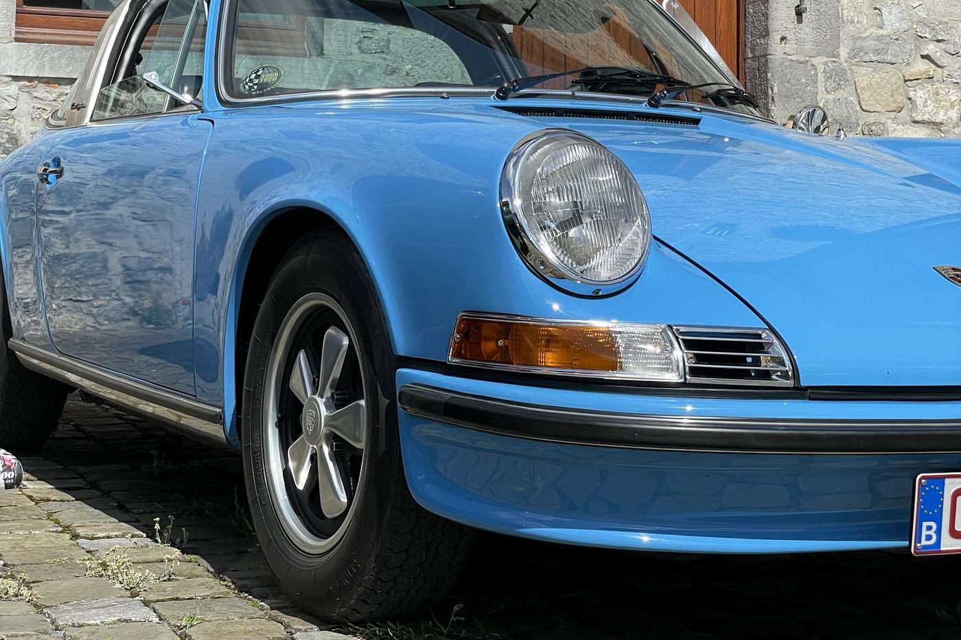 Aile avant et phare rond de la Porsche 911 E Targa bleu clair, sur des pavés
